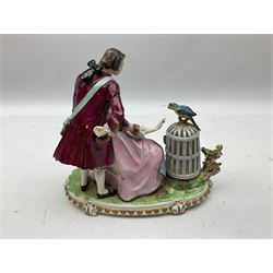 Late 19th/early 20th century Sitzendorf figure group, modelled as a courting couple, the female figure seated offering berries to a parrot stood atop an open bird cage, upon a naturalistically modelled base detailed with encrusted flowers, and further detailed with a gilt foliate band, with blue printed mark beneath, H21.5cm W24cm