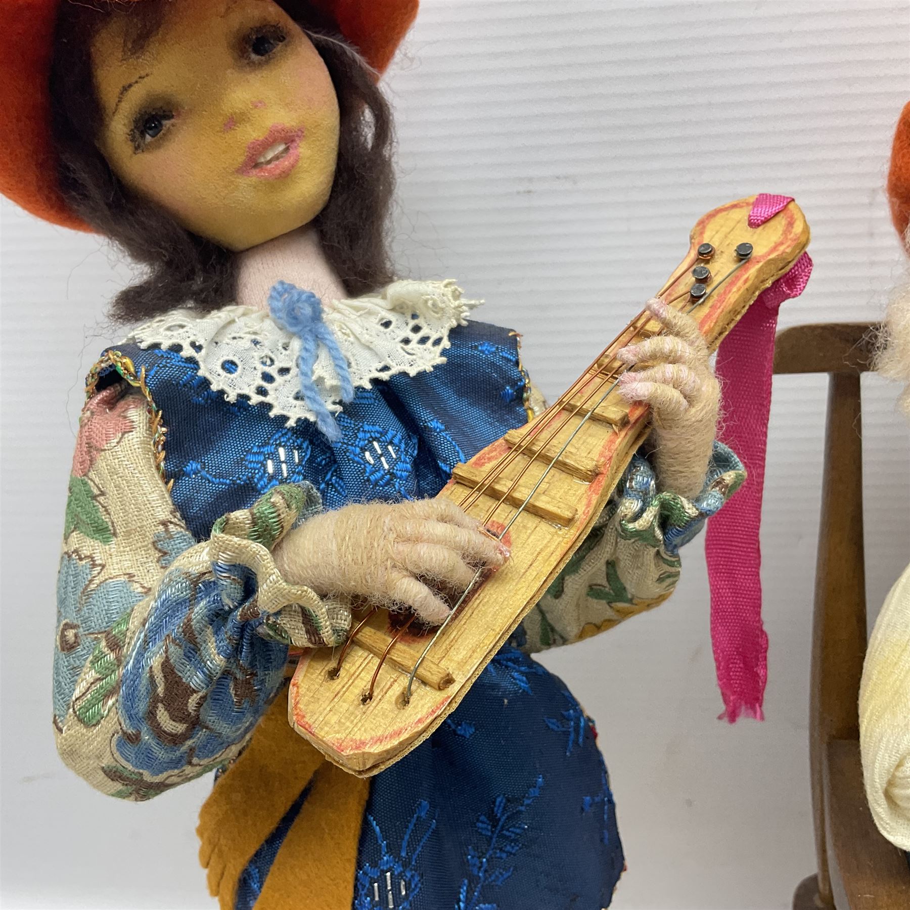 Anna Meszaros Hungary - three hand made needlework figurines - 'The Cobbler' as a child seated in a wooden rocking chair working on a removed boot H28cm; young girl in a long floral dress standing playing a harp H35cm; and young girl wearing a blue tabard standing playing a lute (3) Auctioneer's Note: Anna Meszaros came to England from her native Hungary in 1959 to marry an English businessman she met while demonstrating her art at the 1958 Brussels Exhibition. Shortly before she left for England she was awarded the title of Folk Artist Master by the Hungarian Government. Anna was a gifted painter of mainly portraits and sculptress before starting to make her figurines which are completely hand made and unique, each with a character and expression of its own. The hands, feet and face are sculptured by layering the material and pulling the features into place with needle and thread. She died in Hull in 1998.  