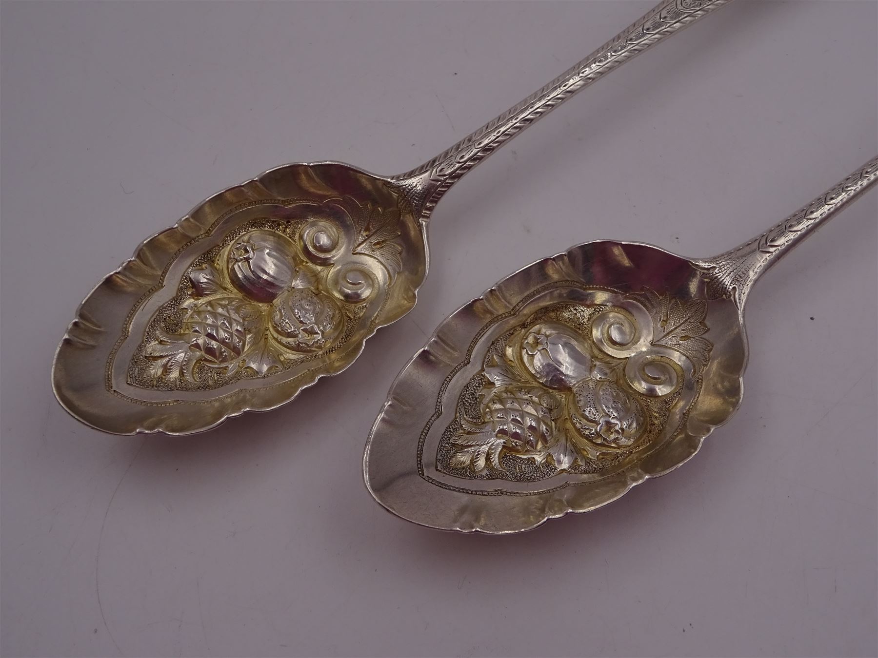 George IV silver fruit serving spoon, the bowl embossed with fruits, with engraved vine leaf decoration to handle, hallmarked London 1789, together with a very similar earlier example, hallmarks worn and indistinct