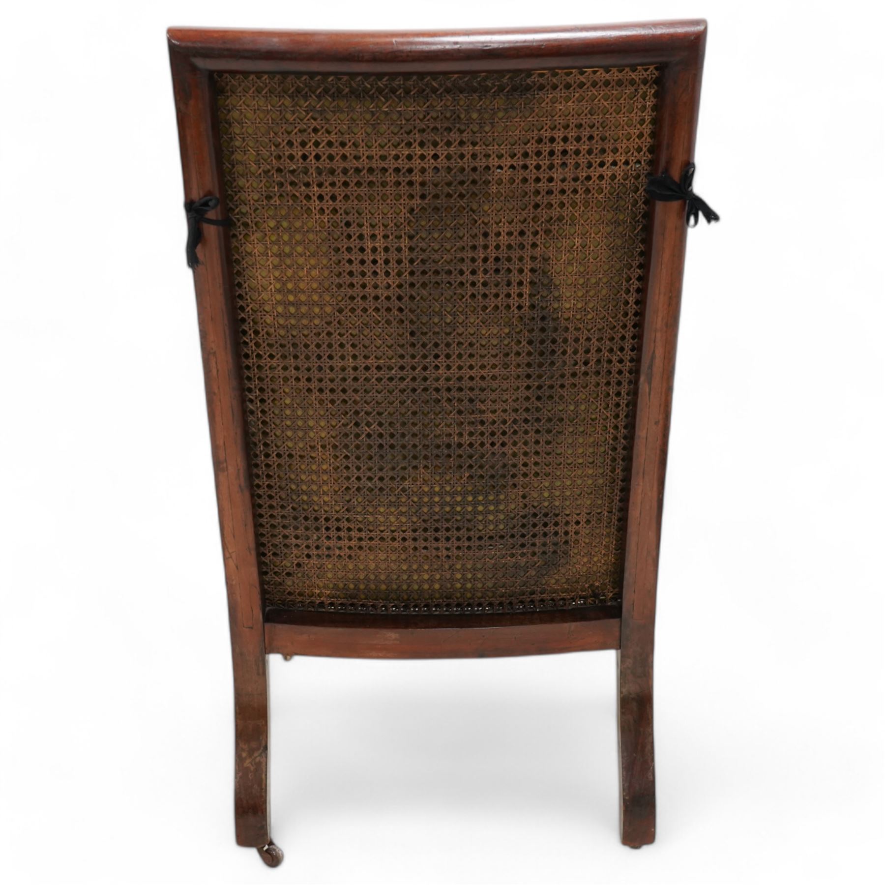 George IV mahogany framed library reading chair, reed moulded frame with cane work seat, back and sides, with loose cushions upholstered in green buttoned leather, upholstered arm rests, turned arm supports terminating to turned and reed carved feet, on castors 