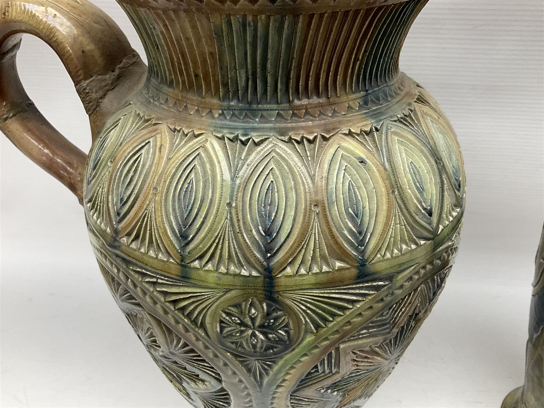 Early 20th century Royal Doulton stoneware vase, decorated with a stylized floral design below a wavy rim, monogrammed B.N, possibly for Bessie Newbery, H28cm, together with an early 20th century glazed jug, heavily carved throughout (2)