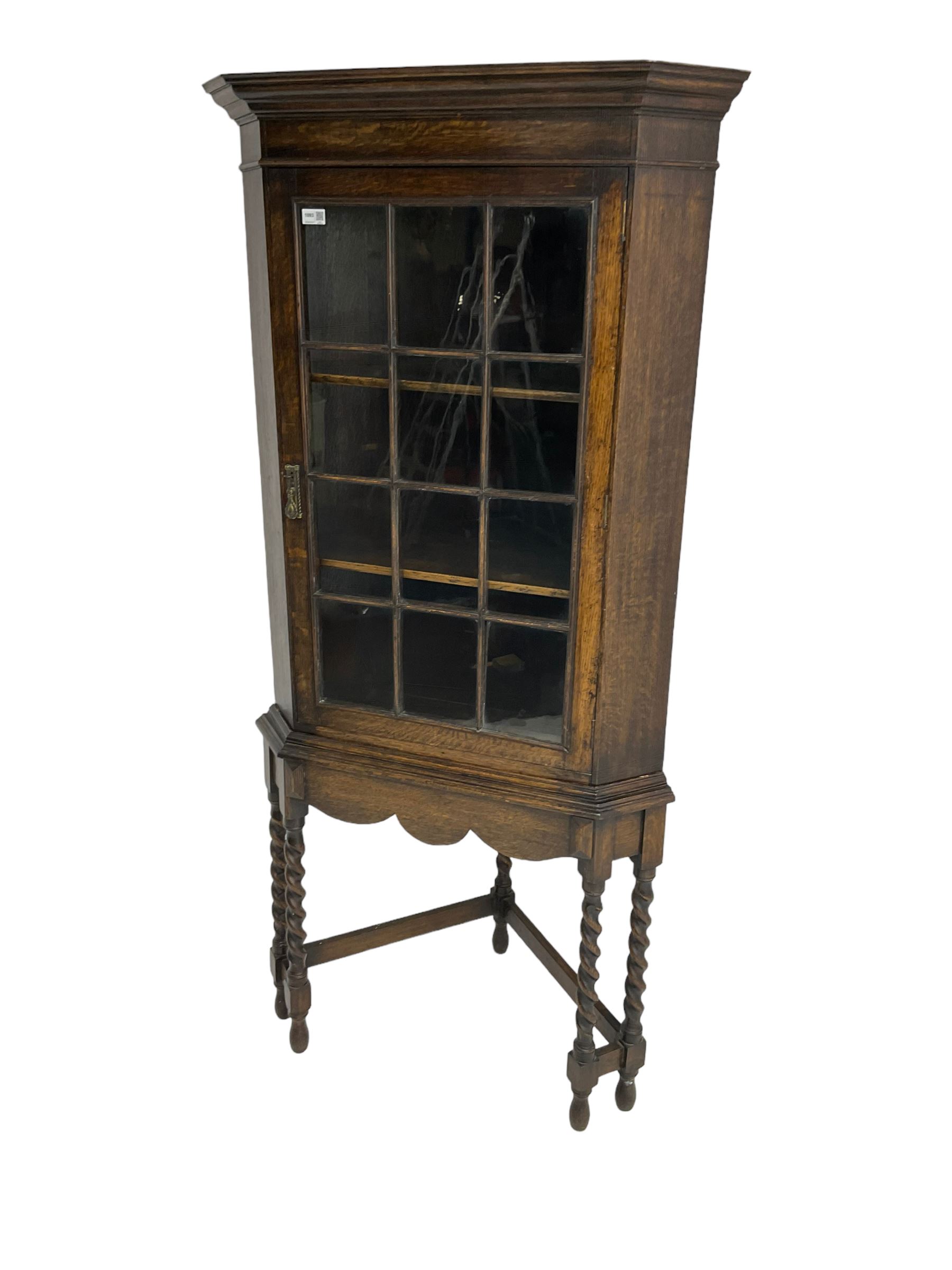 Early to mid-20th century oak corner display cabinet, projecting cornice over astragal glazed door, on spiral turned supports joined by stretchers