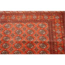 Turkmen hand-knotted carpet, madder red field, with an all-over design of row of Tekke guls, each enclosing stylized cruciform and geometric devices in tones of ivory, dark brown, and indigo, principal border of stylized geometric motifs, flanked by guard border with angular latch hook geometric designs, with cotton fringe ends 