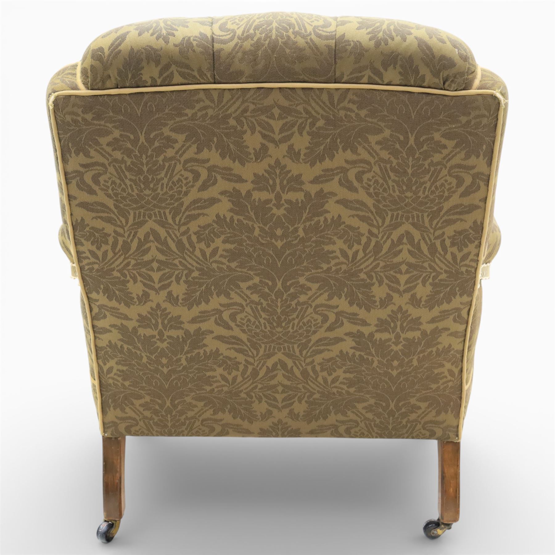 Late Victorian open armchair, in the manner of Howard & Sons, with deep buttoned seat and back upholstered in green damask fabric, with fringed detail to the lower arms, raised upon turned front legs with brass castors