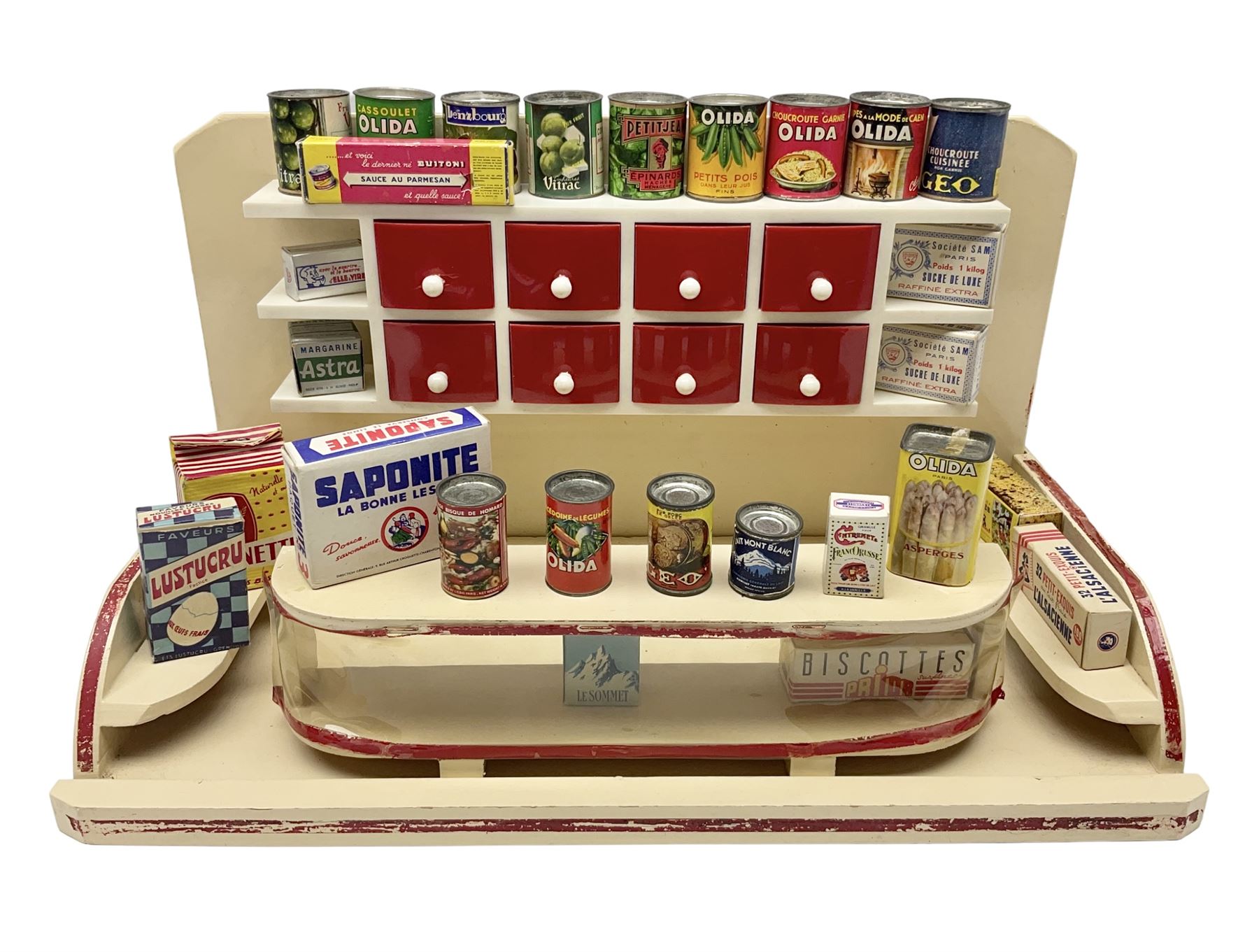 Late 1950s continental red and white painted wooden diorama of a grocery shop interior with fitted shelves and drawers and freestanding 'glazed' counter, fully stocked with miniature tin cans and packets of food L42cm H23cm D22cm