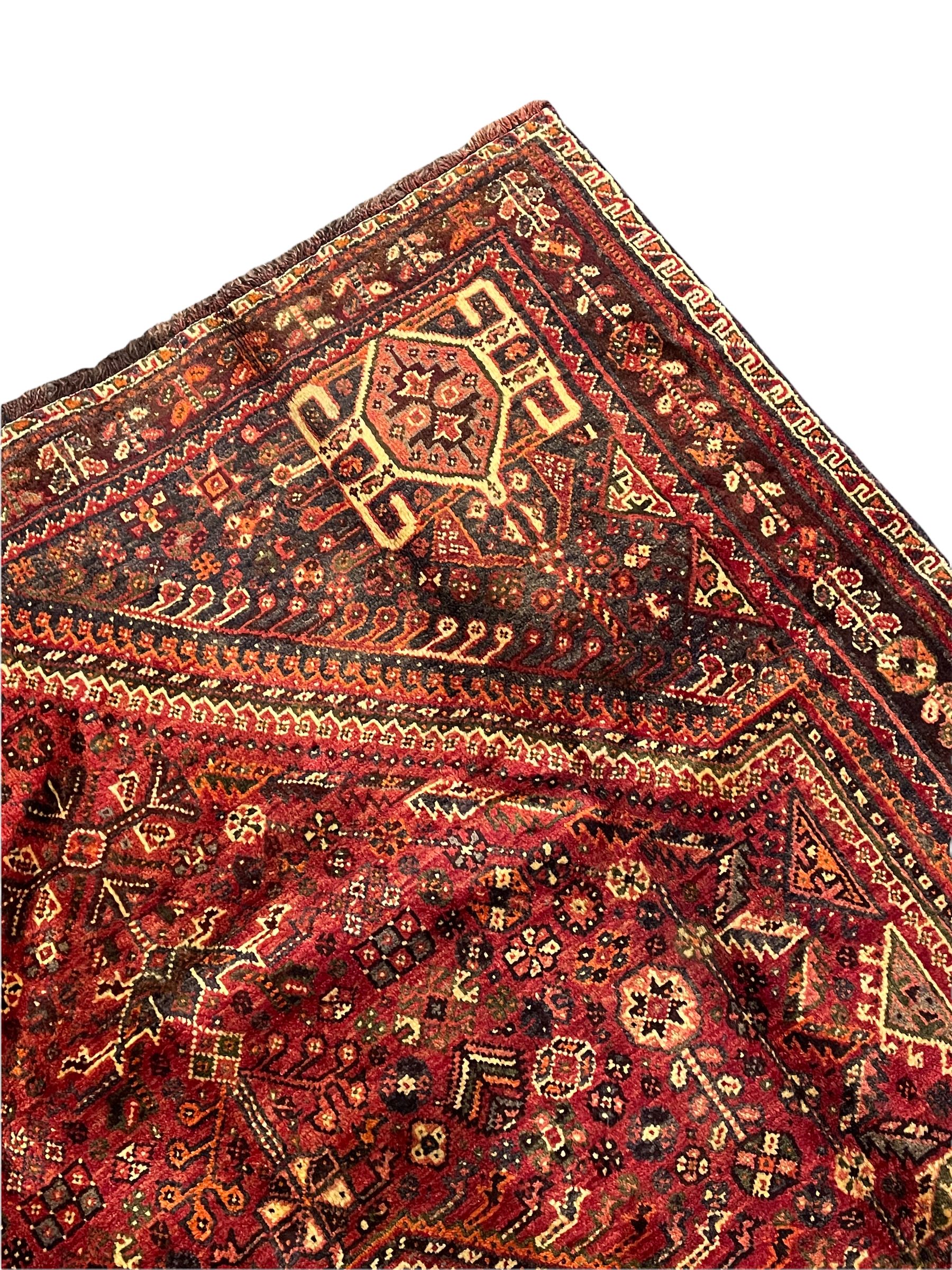 Persian Qashqai red ground rug, the main field decorated profusely with small stylised motifs, central lozenge medallion, multi-band border decorated with trailing foliate and flower head motifs 