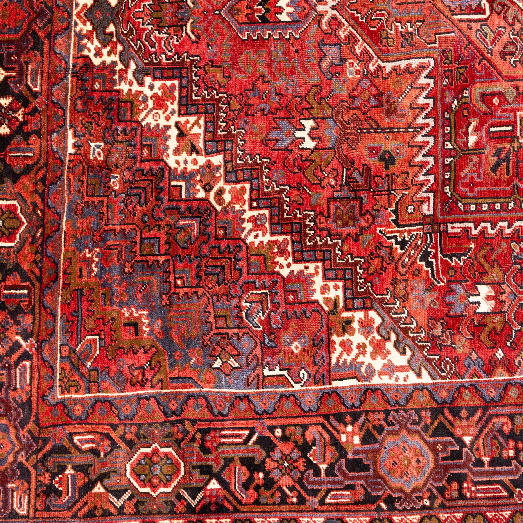North West Persian Heriz hand-knotted carpet, madder red field, with a large central angular star medallion with stepped outlines on ivory ground, surrounded by geometric floral devices and stylized rosettes, with corresponding corner spandrels, enclosed by a bold geometric main border with multiple guard stripes, with cotton fringe ends 