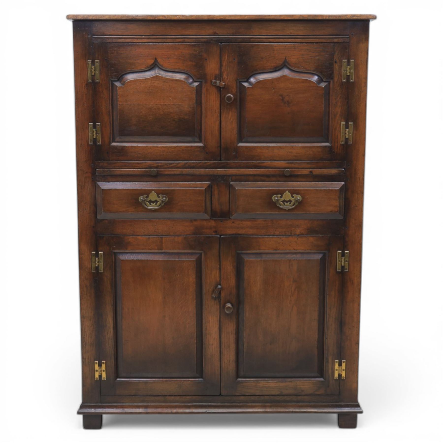  Late 20th century oak four door cupboard in the manner of Titchmarsh and Goodwin, rectangular plank top above two pairs of fielded panel doors with shaped raised panels, central arrangement of a brushing slide above two short drawers with brass swan neck handles and pierced backplates, enclosed by further pair of panelled cupboard doors, fitted with brass butt hinges and turned wooden knobs, raised on plinth base
