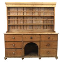 Early 19th century waxed pine farmhouse dresser and rack, the rack featuring two plate shelves and bars above seven drawer base with centre 'dog kennel' recess, raised on turned feet
