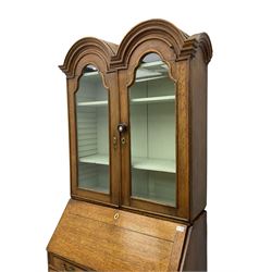 George III oak bookcase on bureau, the double arched top enclosed by two shaped glazed doors, fall-front concealing fitted interior, over four graduating cock-beaded drawers, on bracket feet
