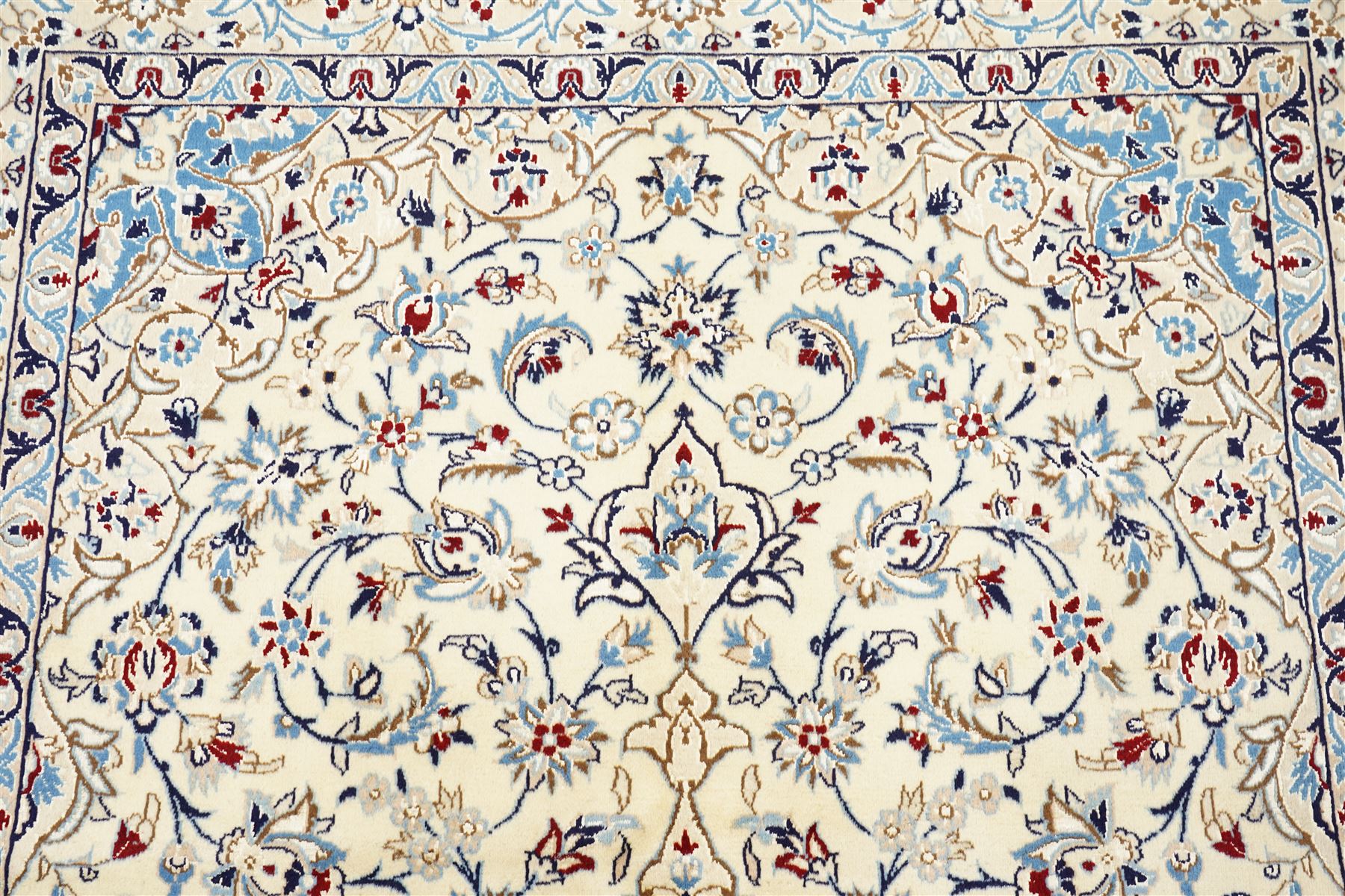 Central Persian Nain hand-knotted rug, ivory field with central medallion in tones of indigo and blue, issuing vinery, palmettes and floral sprays with conforming spandrels, dark blue main border of floral vinery and stylized palmettes, framed by multiple guard borders, with cotton fringe ends 
