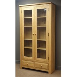 Solid oak large display cabinet, projecting cornice, two bevel eedge glazed doors enclosing four adjustable shelves, two drawers, solid end supports, W100cm, H194cm, D39cm  