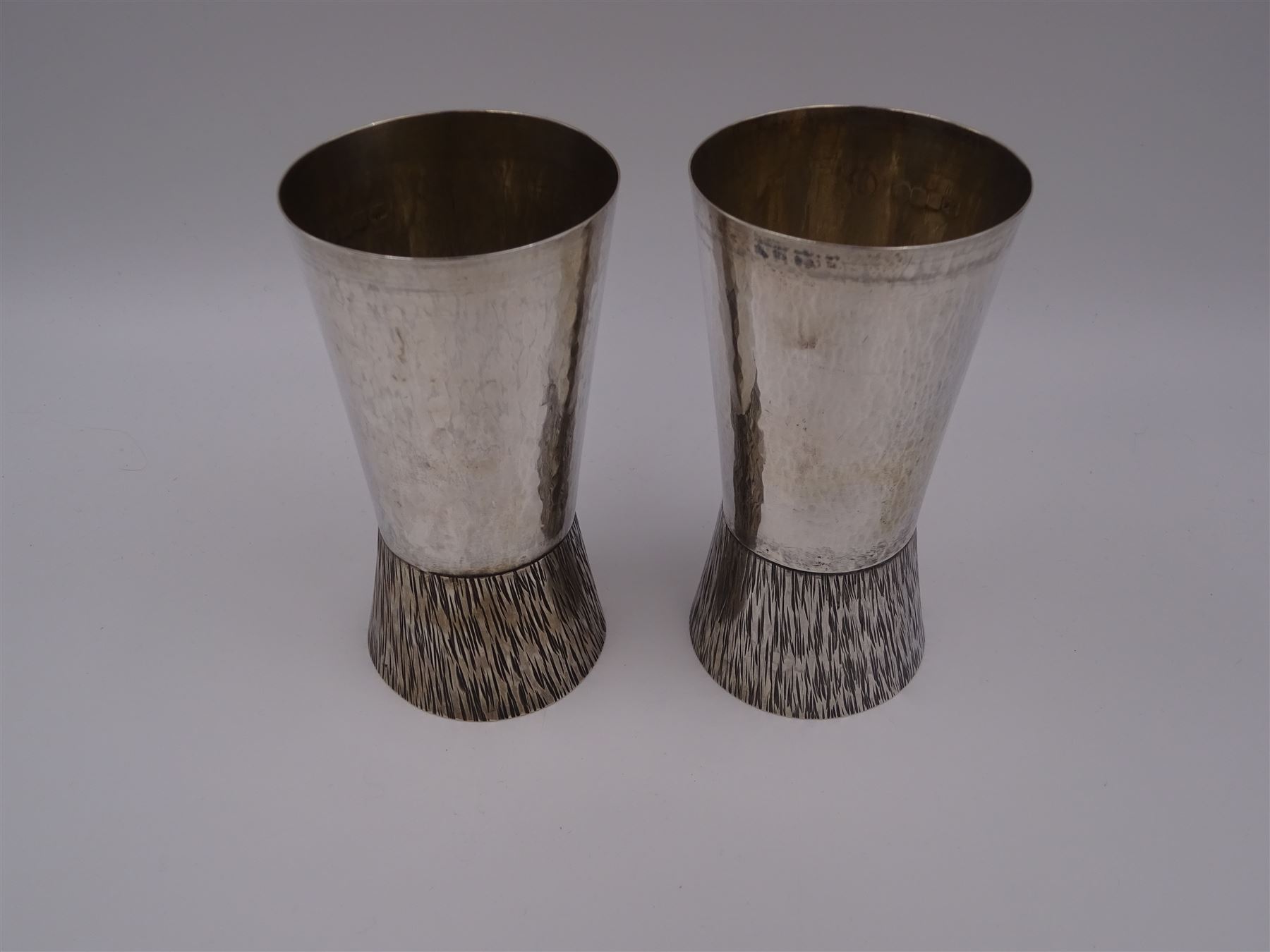 Pair of modern Guild of Hull Silversmiths silver goblets, the bowls each of tapering cylindrical form, with spot hammered finish, upon a tapering foot, etched with abstract lines, hallmarked J & KR, Birmingham 1983, also marked with the three crowns mark of the Guild of Hull Silversmiths, H11.6cm
Notes: Abraham Barachin was the last Hull silversmith to use the Hull mark of three ducal coronets in around 1706. However in 1983 the Assay Offices of Great Britain and the City of Kingston upon Hull granted the Guild of Hull Silversmiths permission to use the City's Coat of Arms as an additional mark on pieces they produced