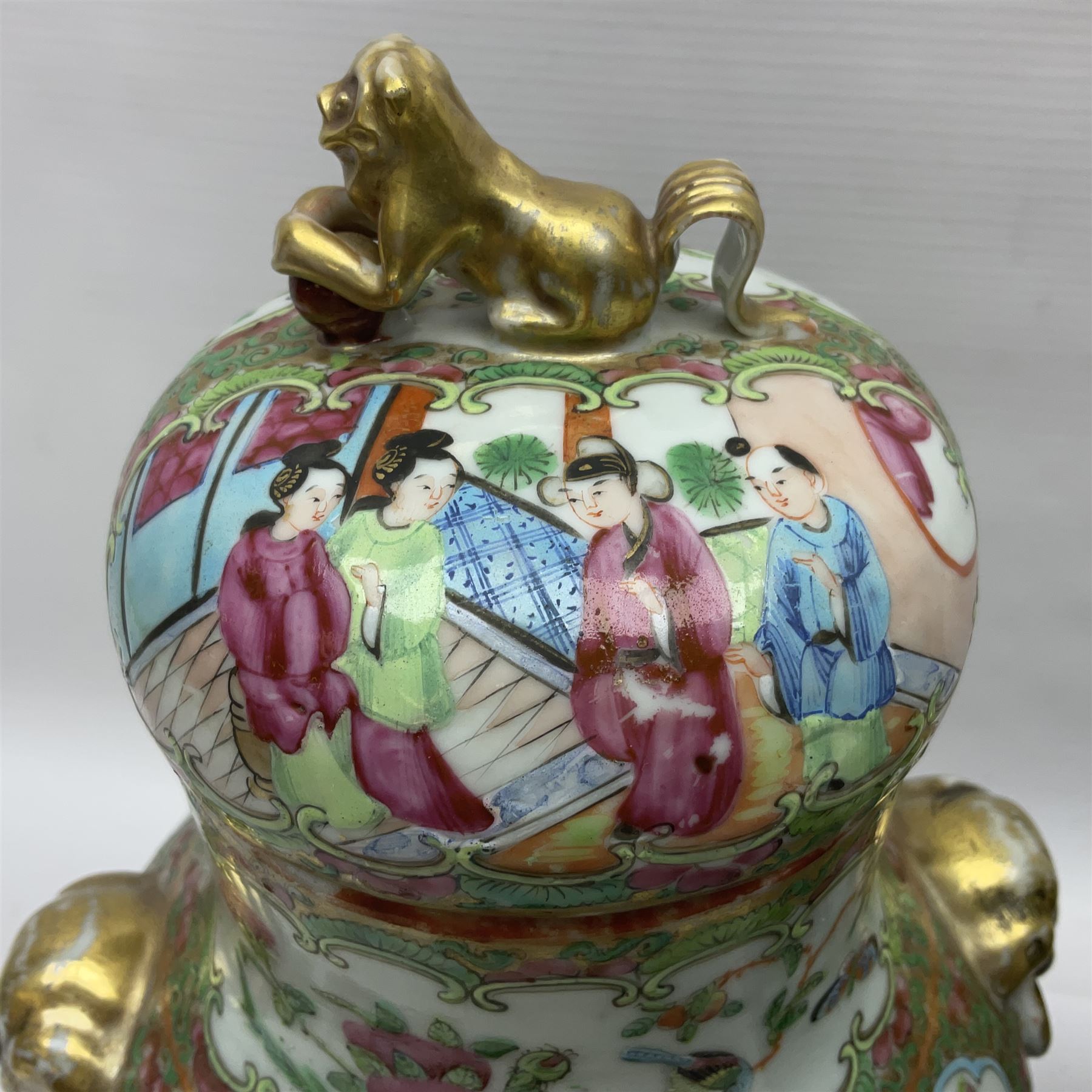 Pair of 19th century Chinese Famille Rose vases and covers, each of baluster form with twin gilt lion mask ring handles to shoulders, the flattened domed covers with gilt temple lion finials, each decorated with alternating reserves of bijin and attendants, and birds and butterflies amongst blossoming peonies, against a gilt ground profusely decorated with stylised scrolls, H32.5cm