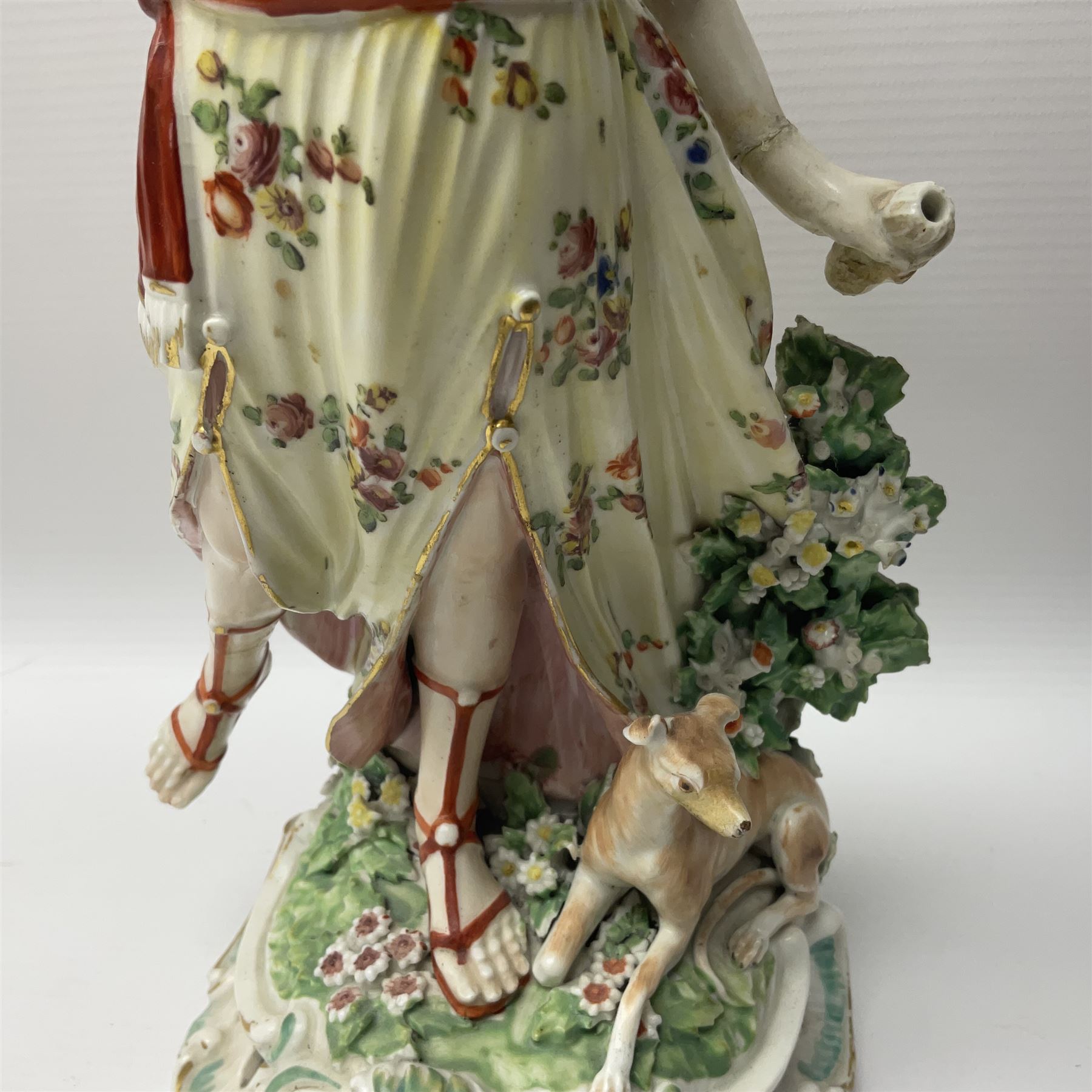 18th century Derby figure of Diana the huntress, circa 1760, modelled reaching for an arrow from quiver across her back, with recumbent hound at her feet, upon a scrolled base with bocage detail, H27.5cm