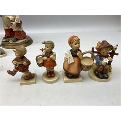 West German style figure modeled as a seated fox, together with seven Hummel figures, to include girl with guitar, boy seated on a fence, girl with basket etc 