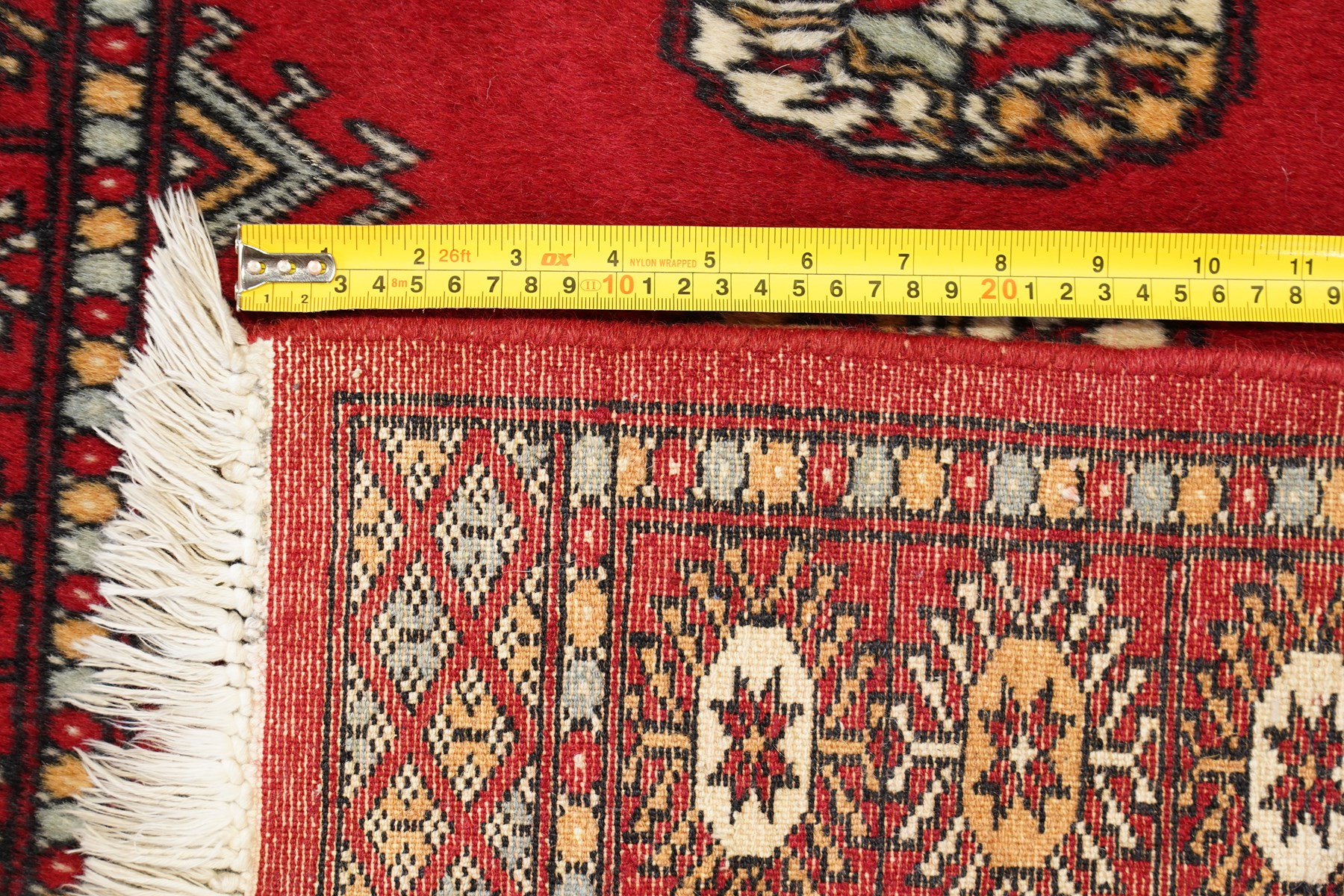 Afghan Bokhara crimson ground carpet, the field decorated with eight Gul motifs with surrounding geometric woven guard bands