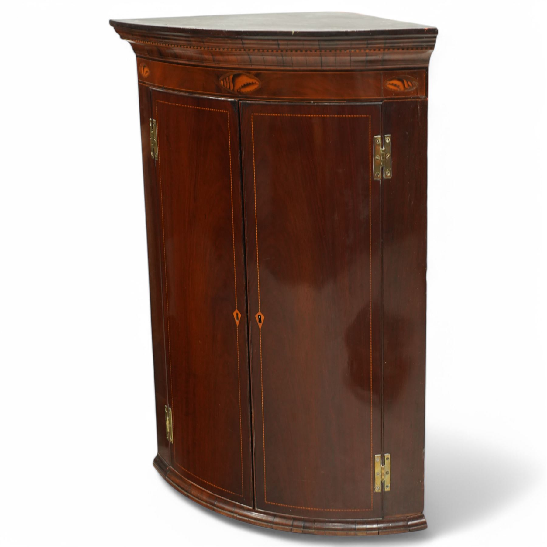 George III inlaid mahogany cylinder corner cupboard, projecting moulded cornice over figured frieze inlaid with shell motifs, two doors with checkered stringing enclosing three shelves, circa 1800