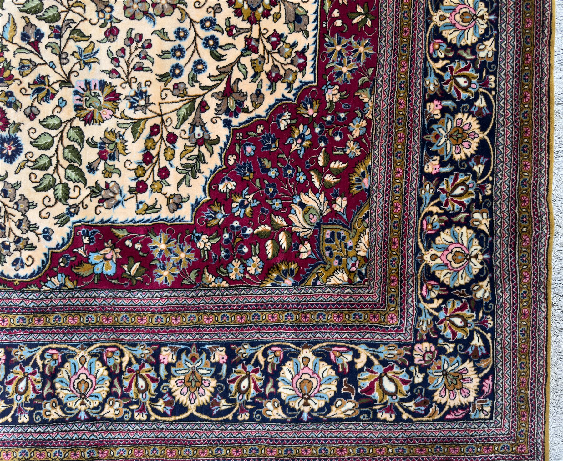 Central Persian Ghom hand-knotted rug, ivory field with scrolling vines, palmettes and flowerheads around a central lobbed medallion with pendants, framed by burgundy spandrels and a navy border of rosettes and arabesques, 289cm x 214cm