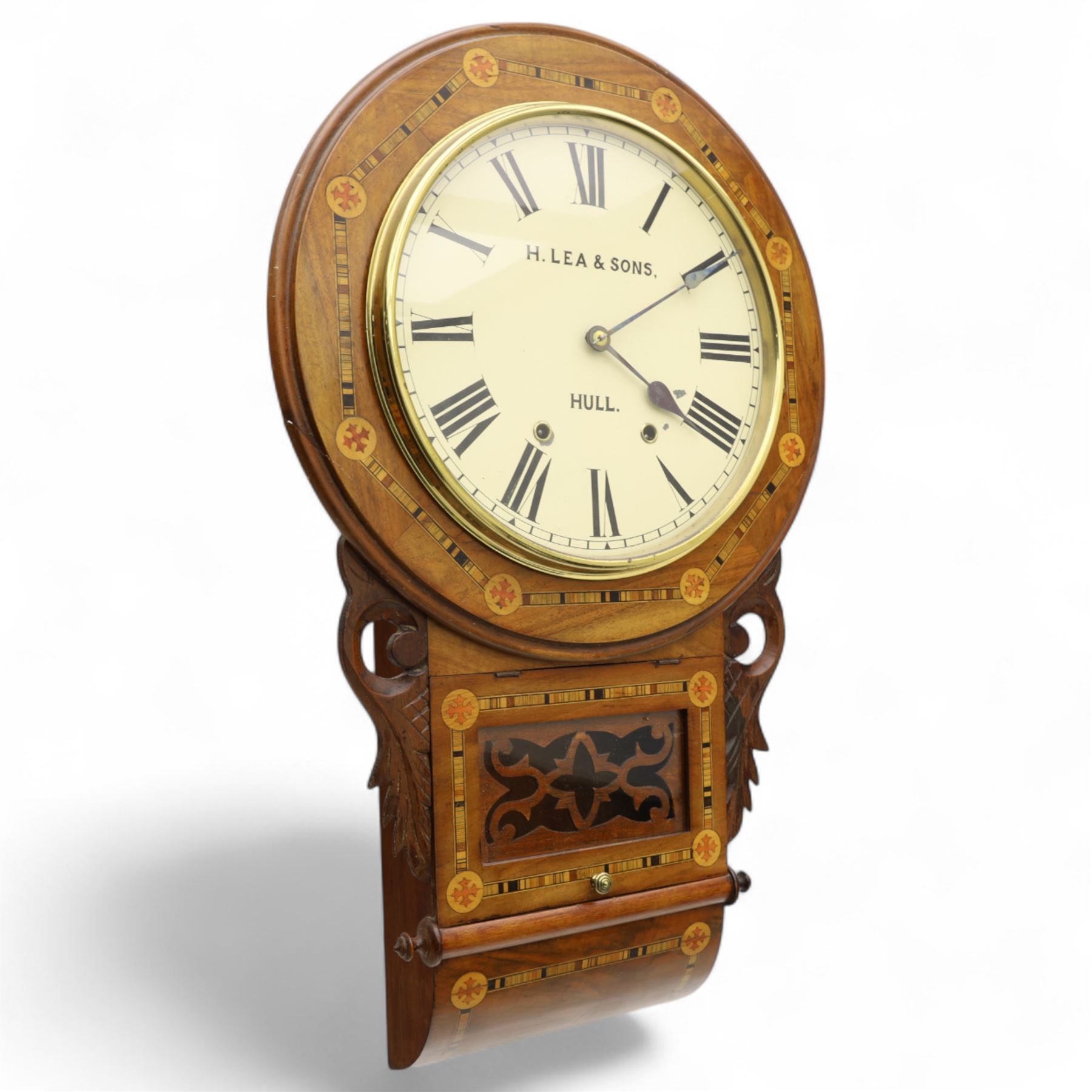 Lea & Son of Hull-American 8-day inlaid mahogany wall clock, with a curved base and carved ears flanking a glazed case door with open fretwork, 12” painted dial with Roman numerals, minute track and spade hands, spring driven movement with a countwheel strike, striking the hours on a bell. With pendulum.
