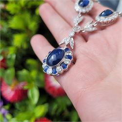 18ct white gold sapphire and diamond milgrain set necklace, oval cabochon cut sapphire surrounded by eight round brilliant cut diamonds and eight French cut sapphires, suspending from a diamond set leaf pendant, single round brilliant cut diamond and a larger old cut diamond, the chain set with six graduating cabochon cut sapphires, each surrounded by diamonds and spaced by a single diamond and a diamond set leaf, to a belcher link chain necklace, hallmarked, total sapphire weight approx 27.00 carat, total diamond weight approx 7.50 carat