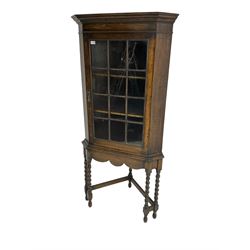 Early to mid-20th century oak corner display cabinet, projecting cornice over astragal glazed door, on spiral turned supports joined by stretchers