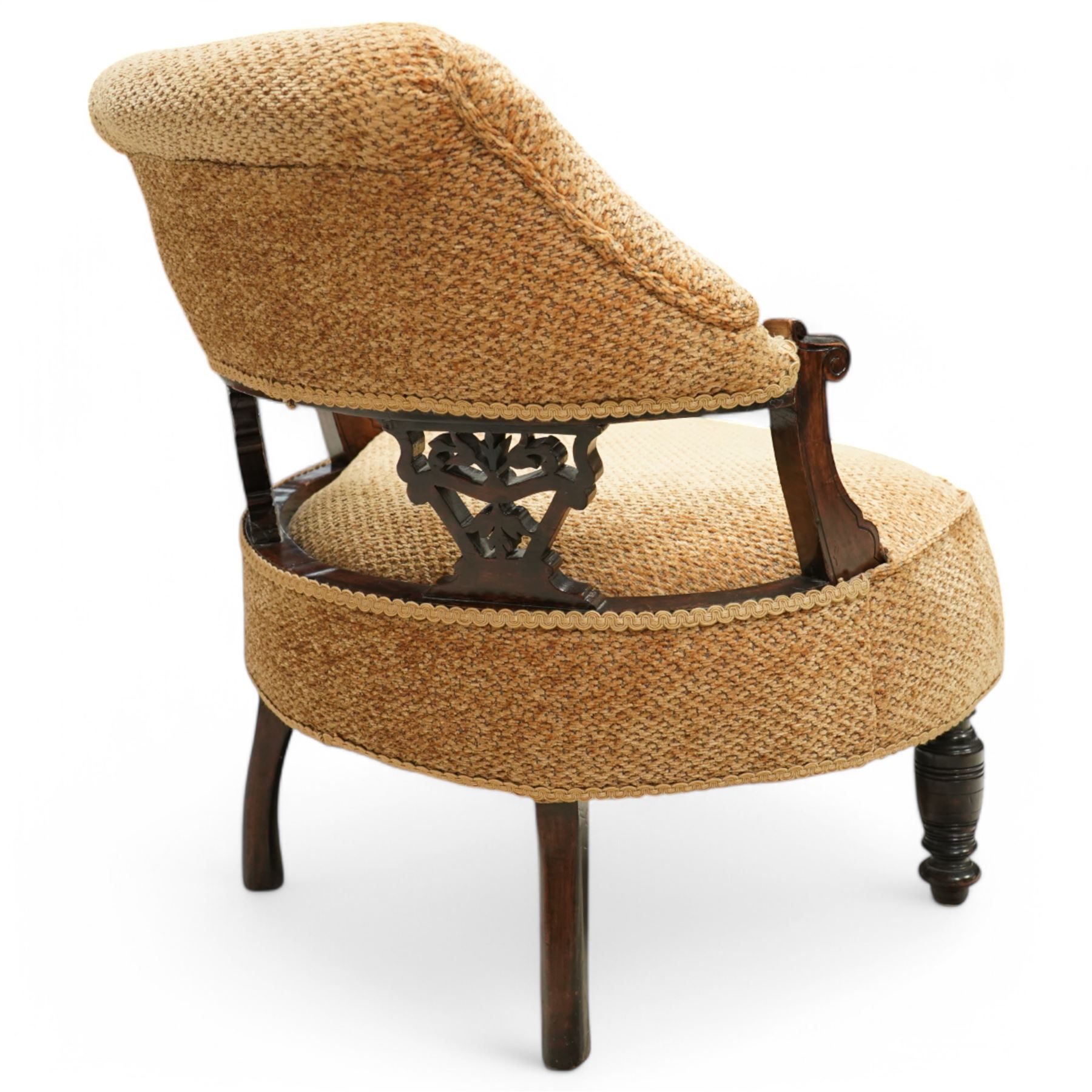 Late Victorian mahogany framed tub shaped chair, curved padded back and overstuffed seat in textured ochre fabric, pierced mahogany back supports with foliate and scroll carving, on turned front legs