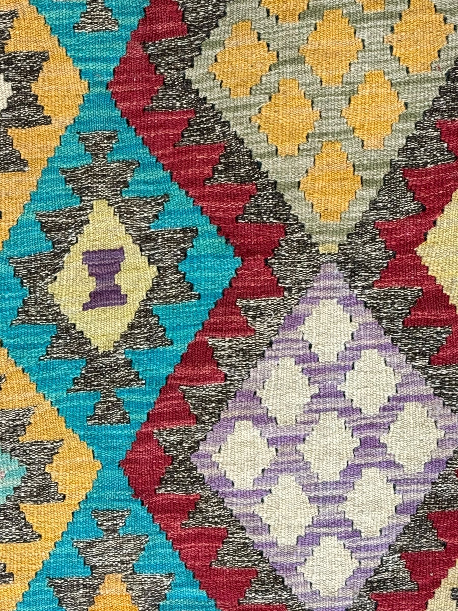 Anatolian Kilim cream ground rug, decorated with repeating diamond motifs in red, blue, yellow, and green, bordered by narrow bands of stylised geometric patterns in contrasting shades