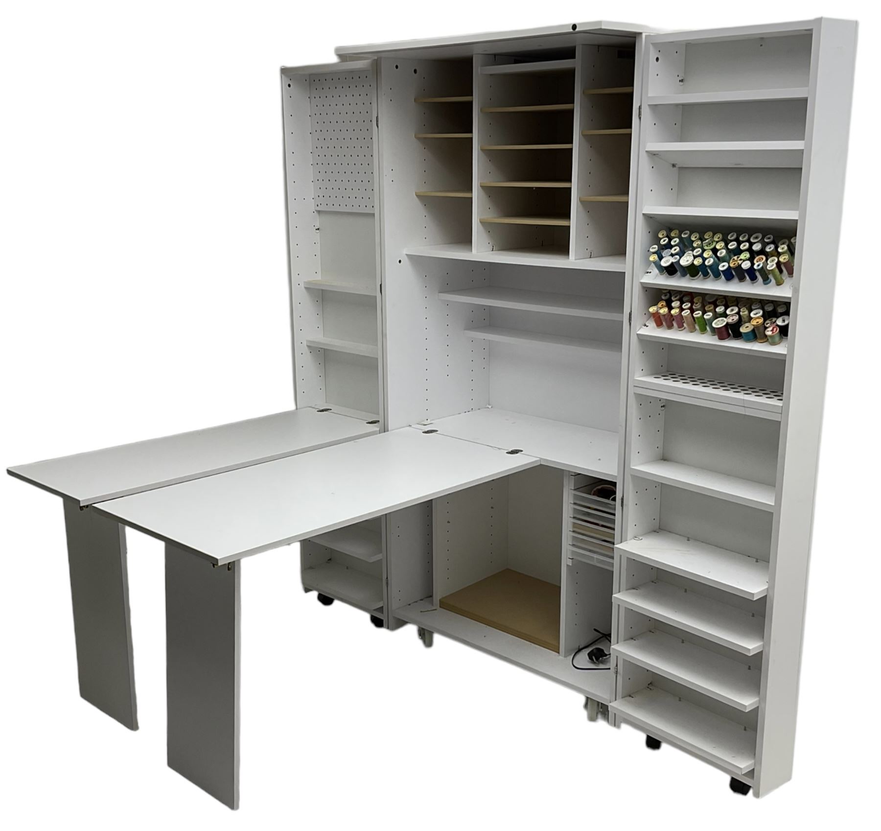 Large white finish sewing cabinet, enclosed by two doors fitted with thread holders and shelves, the interior fitted with shelves and sliding trays, with fold down work surfaces 