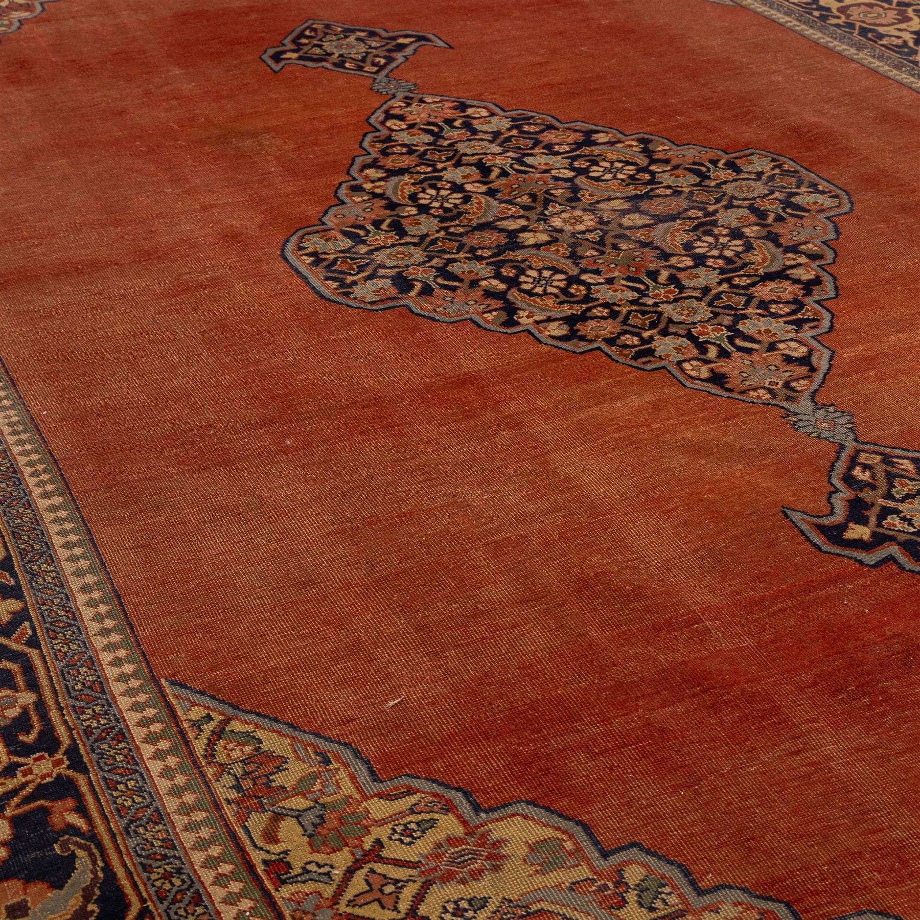 North West Persian Tabriz hand-knotted carpet, salmon field with central elongated lozenge medallion intricately filled with scrolling arabesques and palmettes, framed by stylized corner spandrels within a broad indigo main border  of bold palmettes and floral vinery between multiple guard stripes, rendered in tones of terracotta, sage green, and soft ivory, with cotton fringe ends 