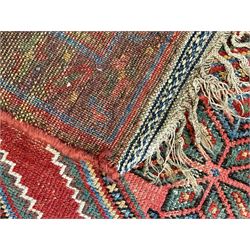 Kurdish crimson ground rug, the field decorated with four lozenge medallions, triple band border decorated with stylised flower heads