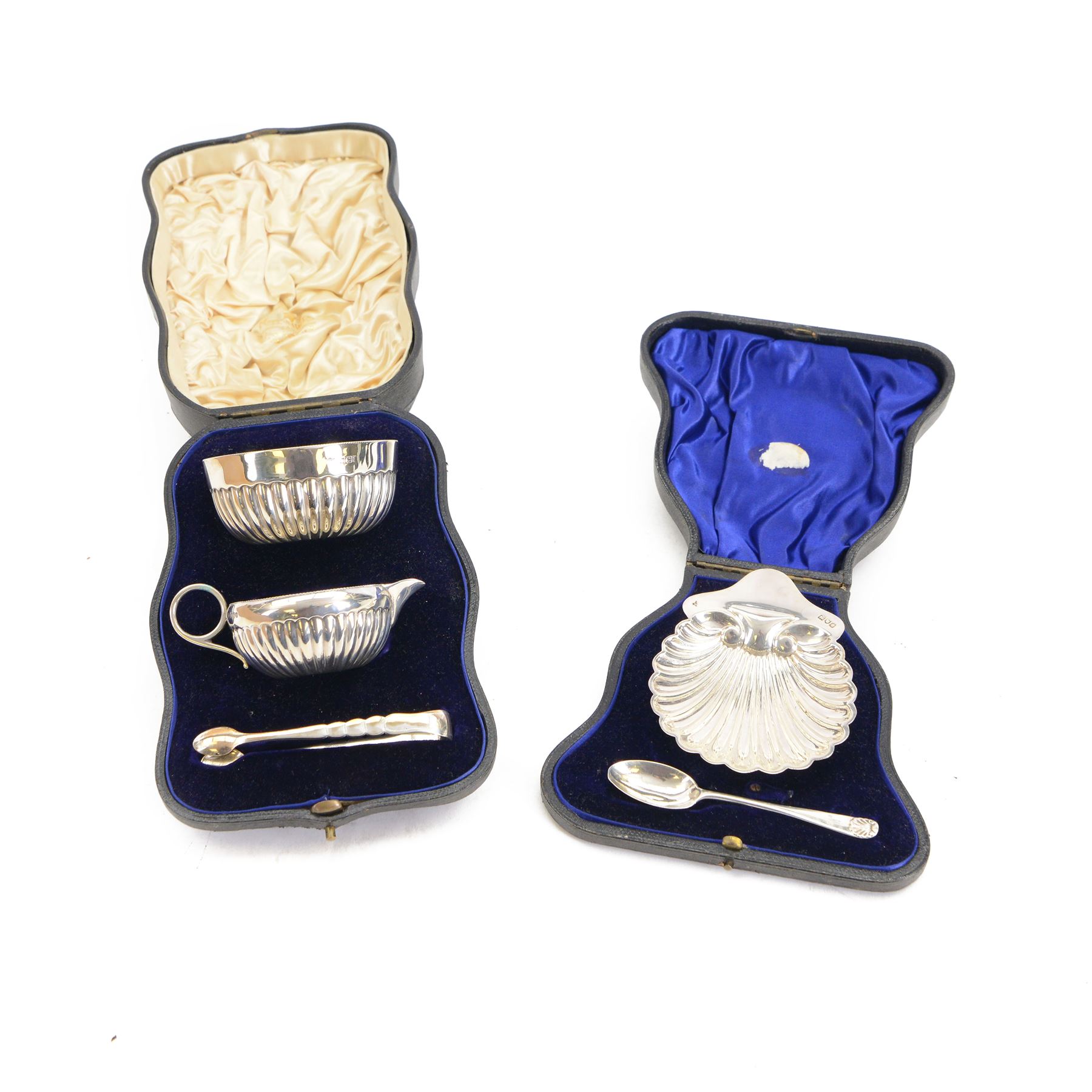 Edwardian silver shell butter dish, upon three bun feet, together with a matching shell spoon engraved with initial, both hallmarked Josiah Williams & Co, London 1906 and 1914, together with an Edwardian milk jug, open sucrier and sugar tongs, the jug and bowl of circular part fluted form with bead rim, hallmarked Mappin & Webb Ltd, Sheffield 1902, both sets contained within fitted tooled leather boxes with silk and velvet lined interiors