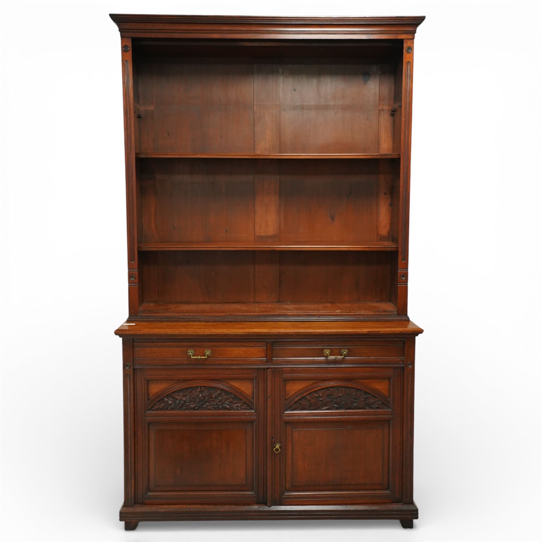 Late Victorian tall walnut open bookcase on cupboard, projecting cavetto cornice over reeded and fluted uprights moulded with roundel motifs, flanking two adjustable shelves, the base fitted with two drawers over panelled cupboards, carved with oakleaf and acorn motifs and grapevines, on bracket feet