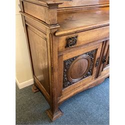 Late 19th century Arts & Crafts period oak mirror back sideboard, shaped bevelled mirror back carved with foliate scrolls and flower heads, down swept supports with elongated club-shaped uprights, moulded rectangular top over two drawers and three cupboards, the drawer fronts with copper handles decorated with sailing ships, panelled doors carved with mythical beasts, flowerheads and foliage, on moulded block feet