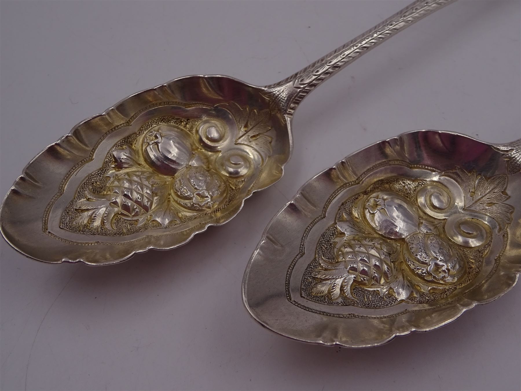 George IV silver fruit serving spoon, the bowl embossed with fruits, with engraved vine leaf decoration to handle, hallmarked London 1789, together with a very similar earlier example, hallmarks worn and indistinct