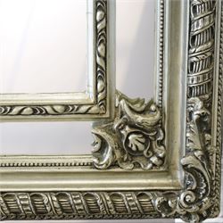 Impressive Baroque Revival mirror in antique silvered finish, the pierced cartouche shell pediment flanked  by C-scrolls and flower heads, the outer frame with ribbon-twist motifs throughout, the central arched bevelled plate surrounded by further rectangular mirror panels with cartouche mounts