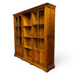 Wesley Barrel - large cherry wood bookcase, with projecting cornice and fielded panelled sides, with three sections comprising three fixed shelves, sliding glazed and panelled doors, moulded plinth base