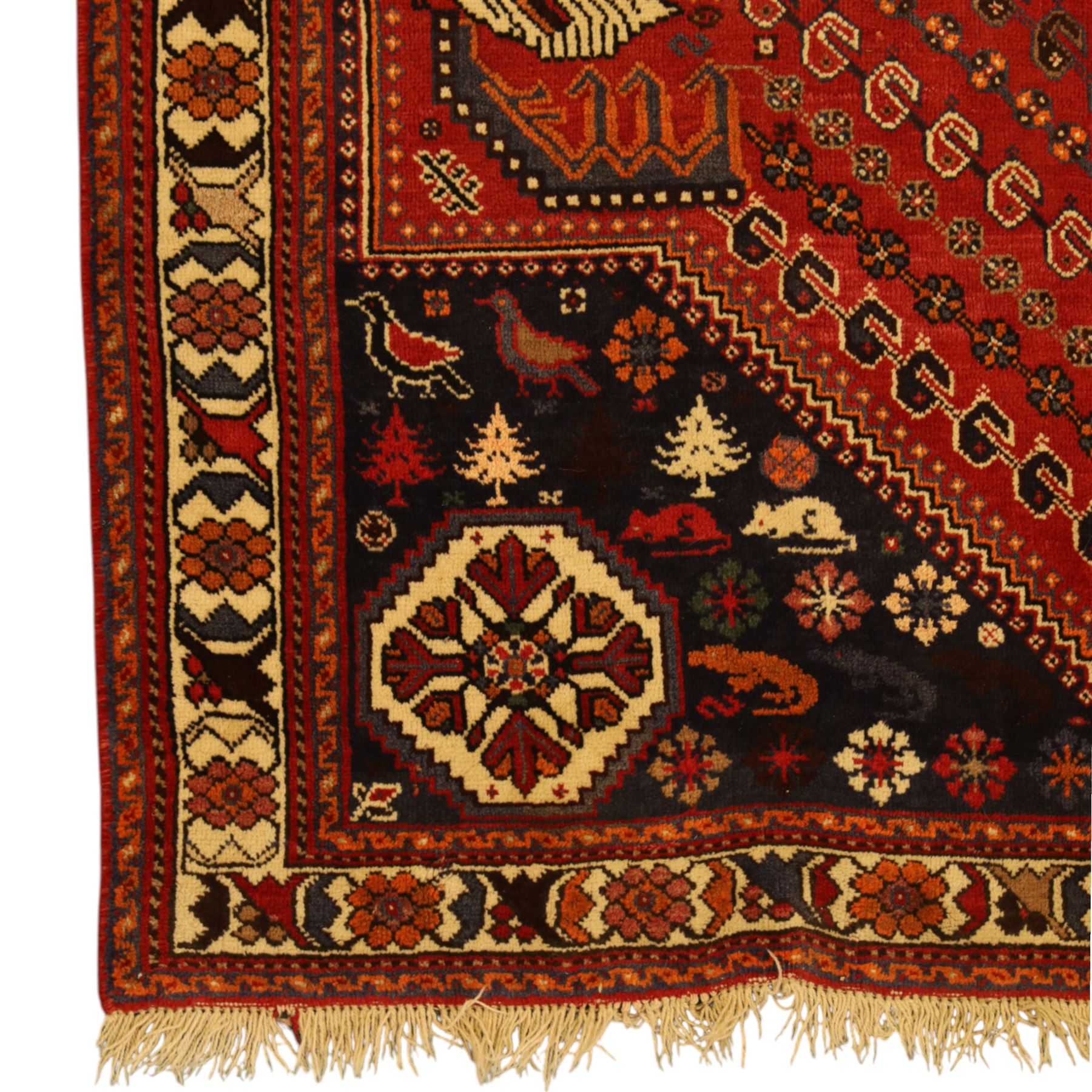Persian Shiraz rug, hand-knotted tribal rug, bold geometric central medallion, set within a large hexagonal crimson field with angular stepped corners in dark blue, with boteh motifs, rosettes, and other tribal symbols arranged in diagonal rows, the corners with indigo spandrels decorated with zoomorphic and arboreal motifs, main border composed of a floral meander motif with large rosette, flanked guard borders with vine and leaf motifs 