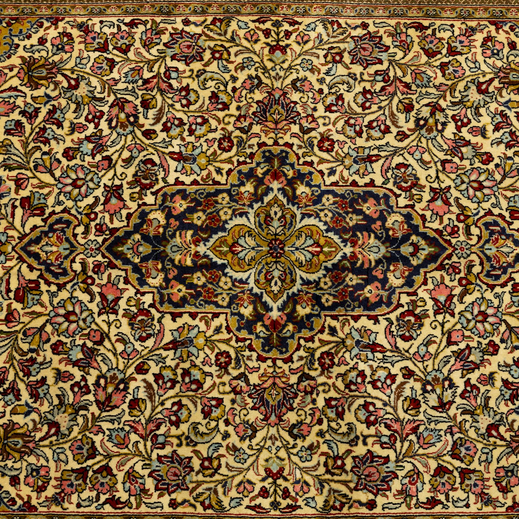 Fine Qom hand-knotted rug, ivory ground, with a dark navy shaped floral medallion and pendants, the field densely worked with fine flowering vines, palmettes and leafy scrolls in red, green, ochre and blue tones, within golden spandrels and a dark navy floral border, flanked by narrow guard stripes, with cotton fringes