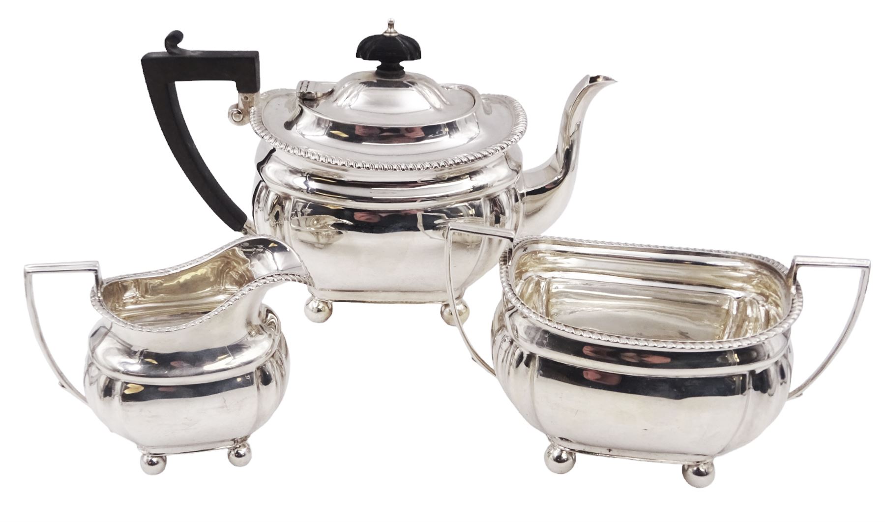 1920s silver three piece bachelors tea service, comprising teapot, cream jug and twin handled open sucrier, each of bellied form with oblique gadrooned rim, upon four bun feet, the teapot with Bakelite type handle and finial, hallmarked Thomas Edward Atkins, Birmingham 1912, teapot H13.5cm
