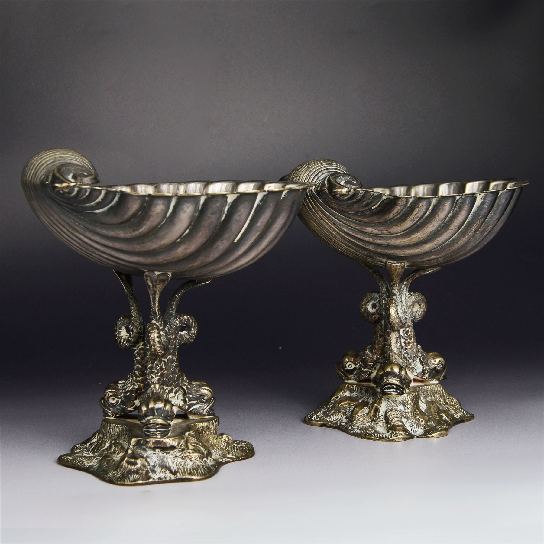Pair of Victorian silver plated comports, with clam shell bowls supported by three dolphins upon a rocky base, H12cm