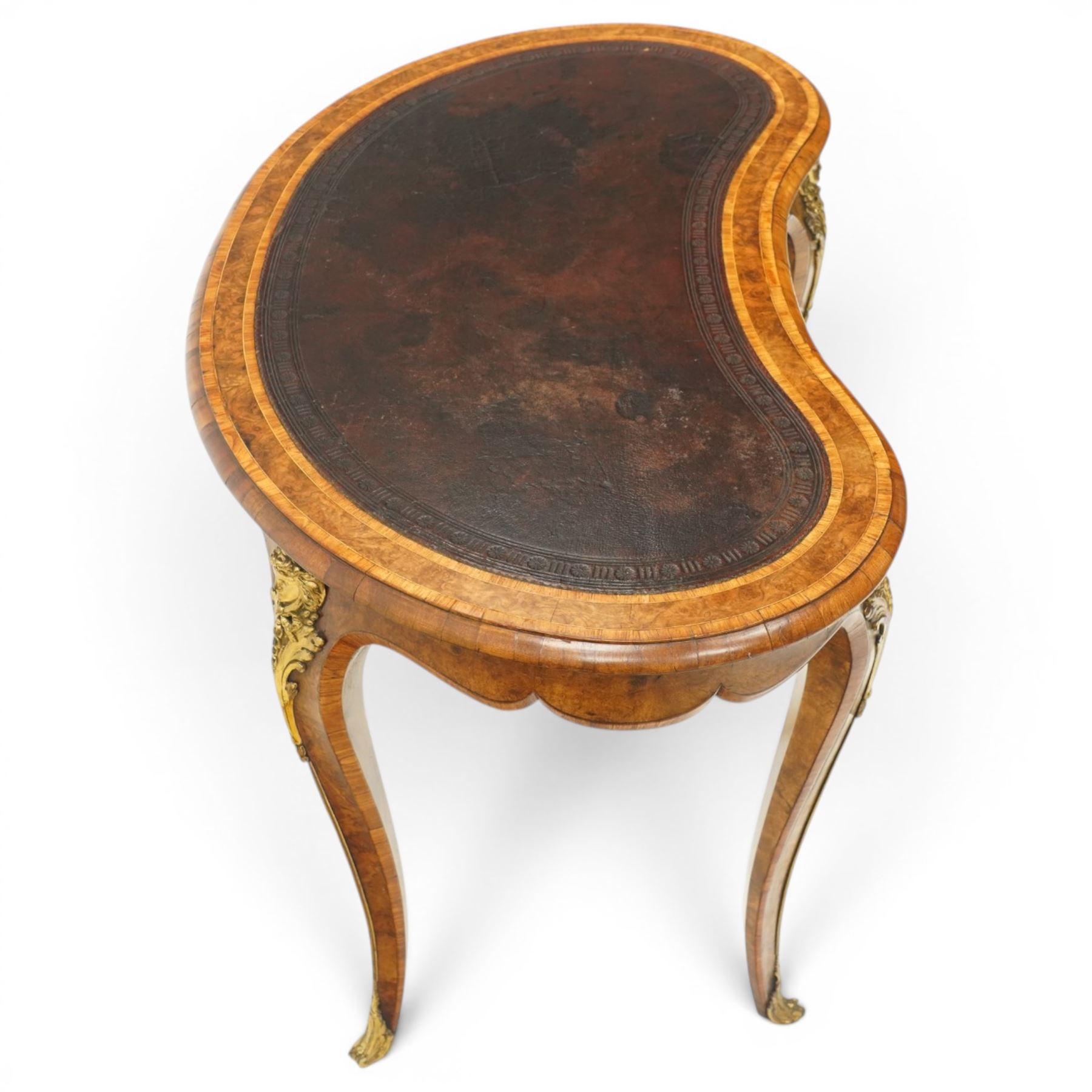 Gillow & Company (1862-1897) - Victorian figured walnut kidney shaped writing table, the shaped top inset with oxblood leather writing surface with embossed edge, surrounded by banded burr-walnut and crossbanding with moulded edge, fitted with single shaped frieze drawer flanked by scalloped side-aprons, raised on tapering and chamfered cabriole supports embellished with ormolu mounts in the forms of maidens over tapering acanthus leaves, the mounts trailing down the front of the legs to terminate to ormolu scroll feet, stamped 'Gillow & Co 3576' to drawer interior