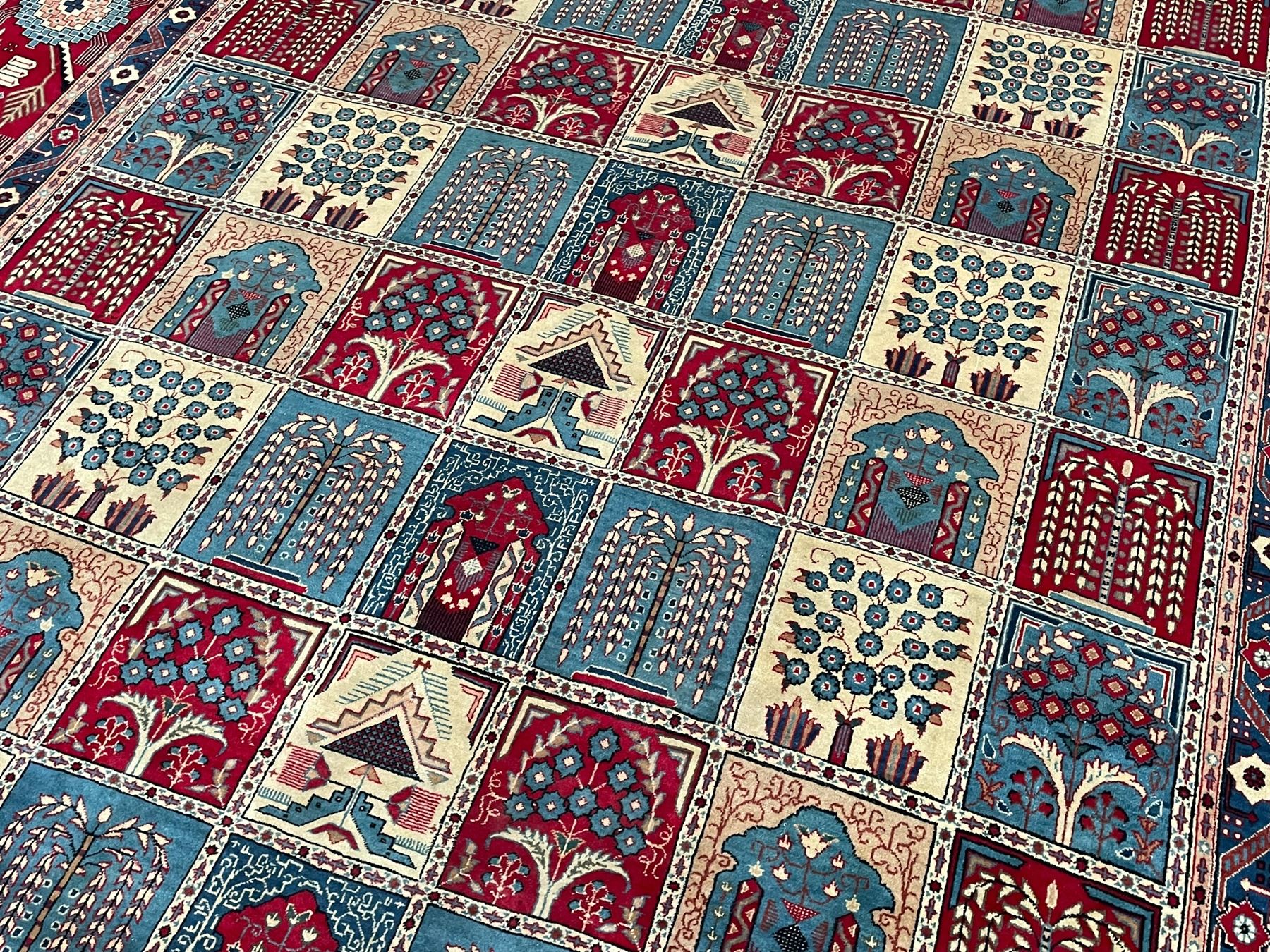 Persian Bakhtiari crimson ground carpet, the field divided into seventy panels decorated tree of life motifs, mihrabs and stylised plants, the border decorated with repeating circular medallions formed of Hac motifs, floral pattern guard stripes 