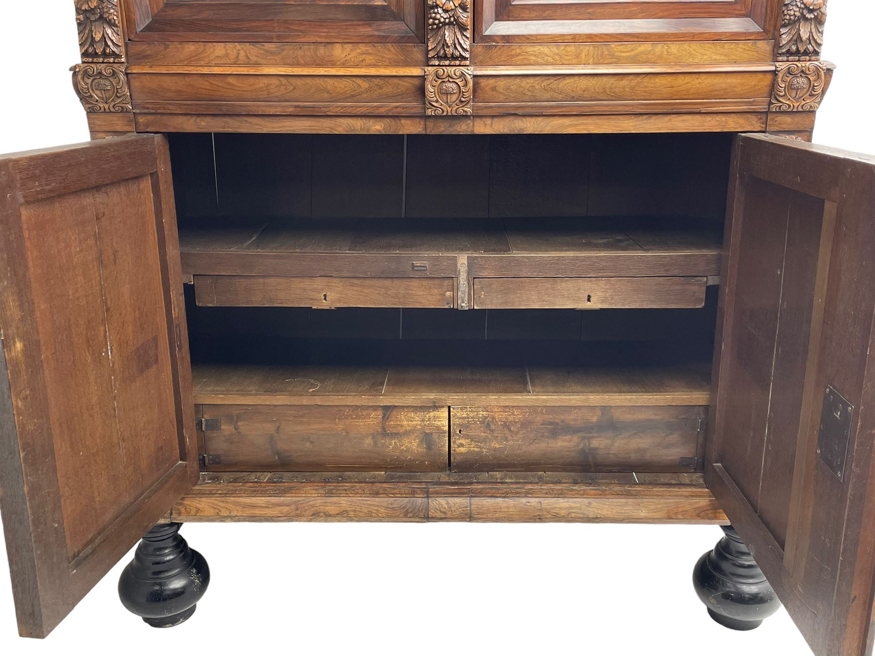 Late 17th century Flemish/Dutch rosewood and oak ‘Zeeuwse Kast’ or cupboard, projecting cornice carved with three putti masks, the uprights carved with lion masks over ribbons, flower heads and foliage, enclosed by four geometric panelled doors, lower central upright carved with flower head over foliate ribbon with bird among foliage, the escutcheon hidden by swivel berry carved cover, interior fitted with shelves, two drawers and shallow hinged cupboard, on two large turned and ebonised feet, circa 1680