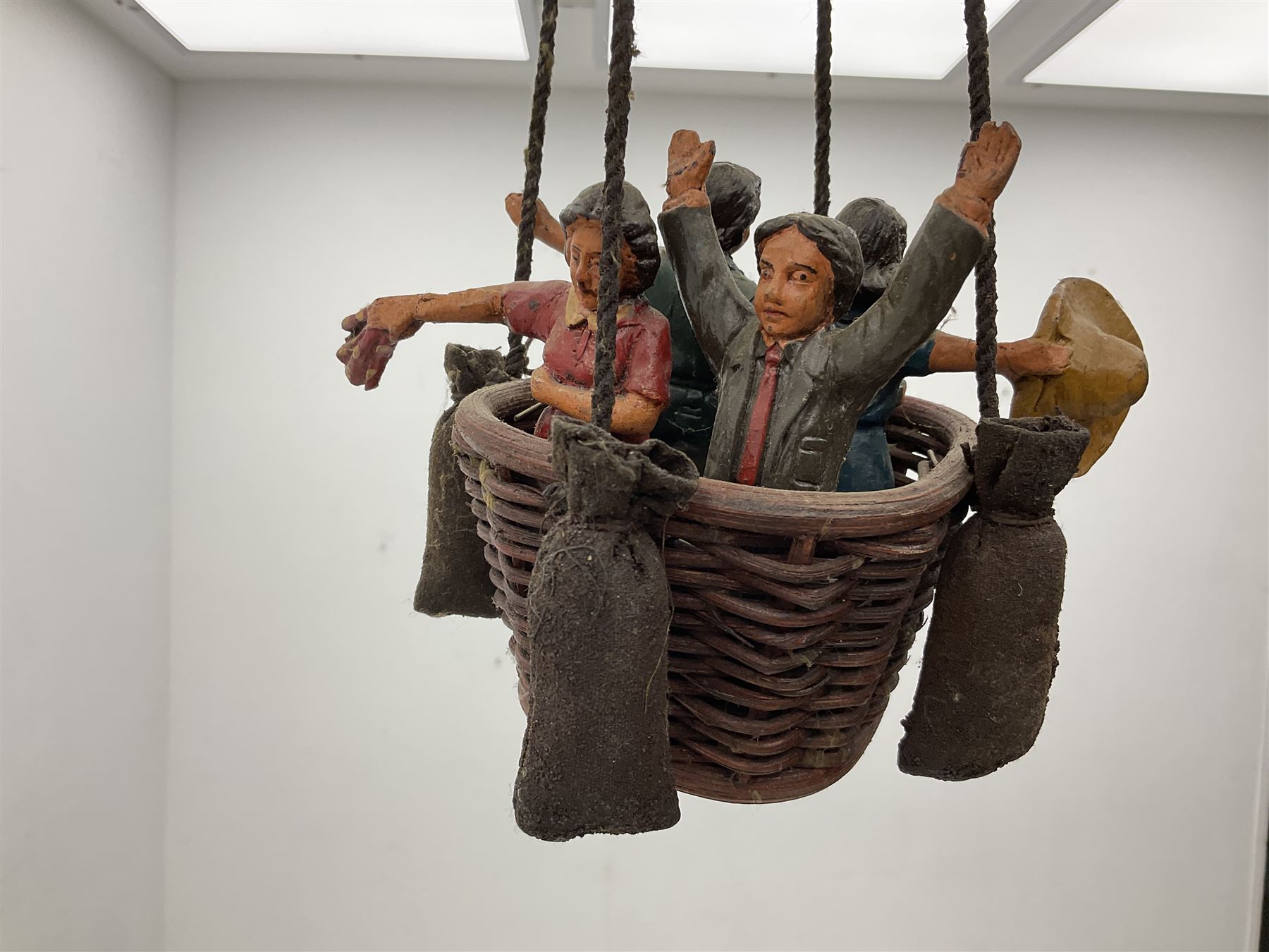 Painted wooden hanging model of a hot air balloon group, the balloon above a wicker basket complete with sandbags and figures, together with a similar example with a clown figure below, H68cm