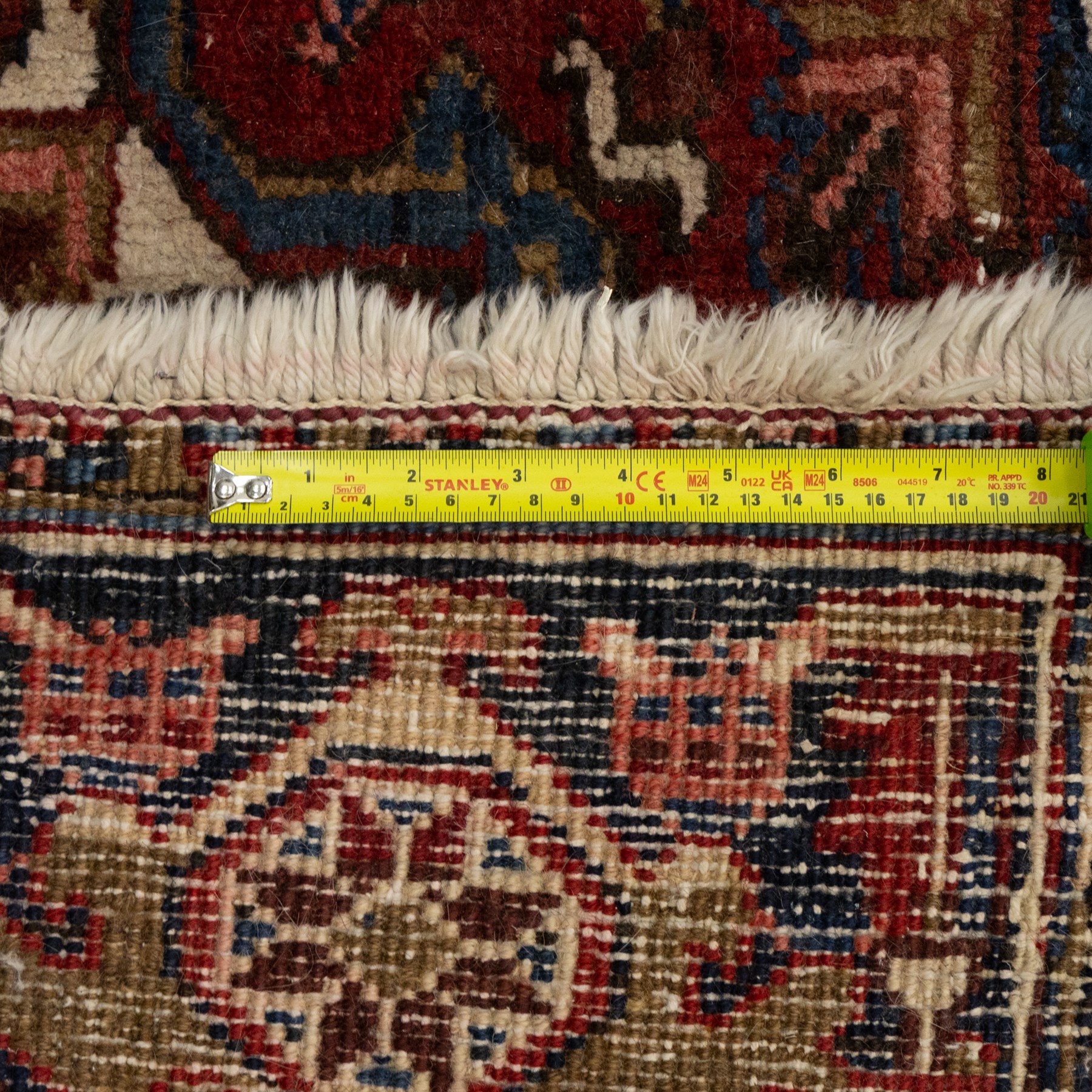 Persian Heriz carpet, red ground with large central geometric medallion, angular flowering branches and stylised foliate decoration, within a broad dark blue floral border and narrow guard stripes
