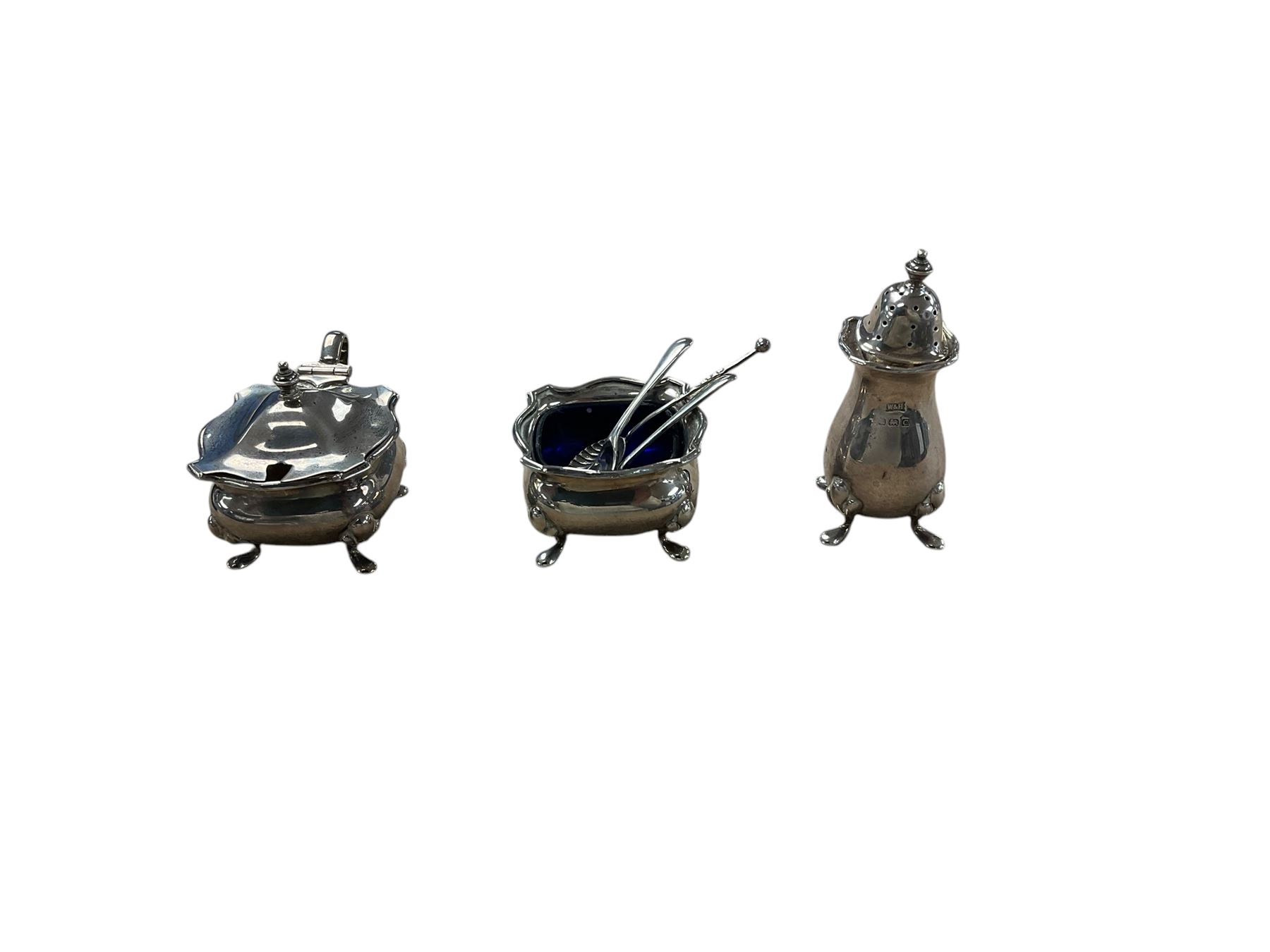 1920s silver three piece part cruet set, comprising pepper shakers, open salt with blue glass liner and a mustard pot, all upon four pad feet, hallmarked White & Hawkins, Birmingham,  , with three silver salt spoons, hallmarked 