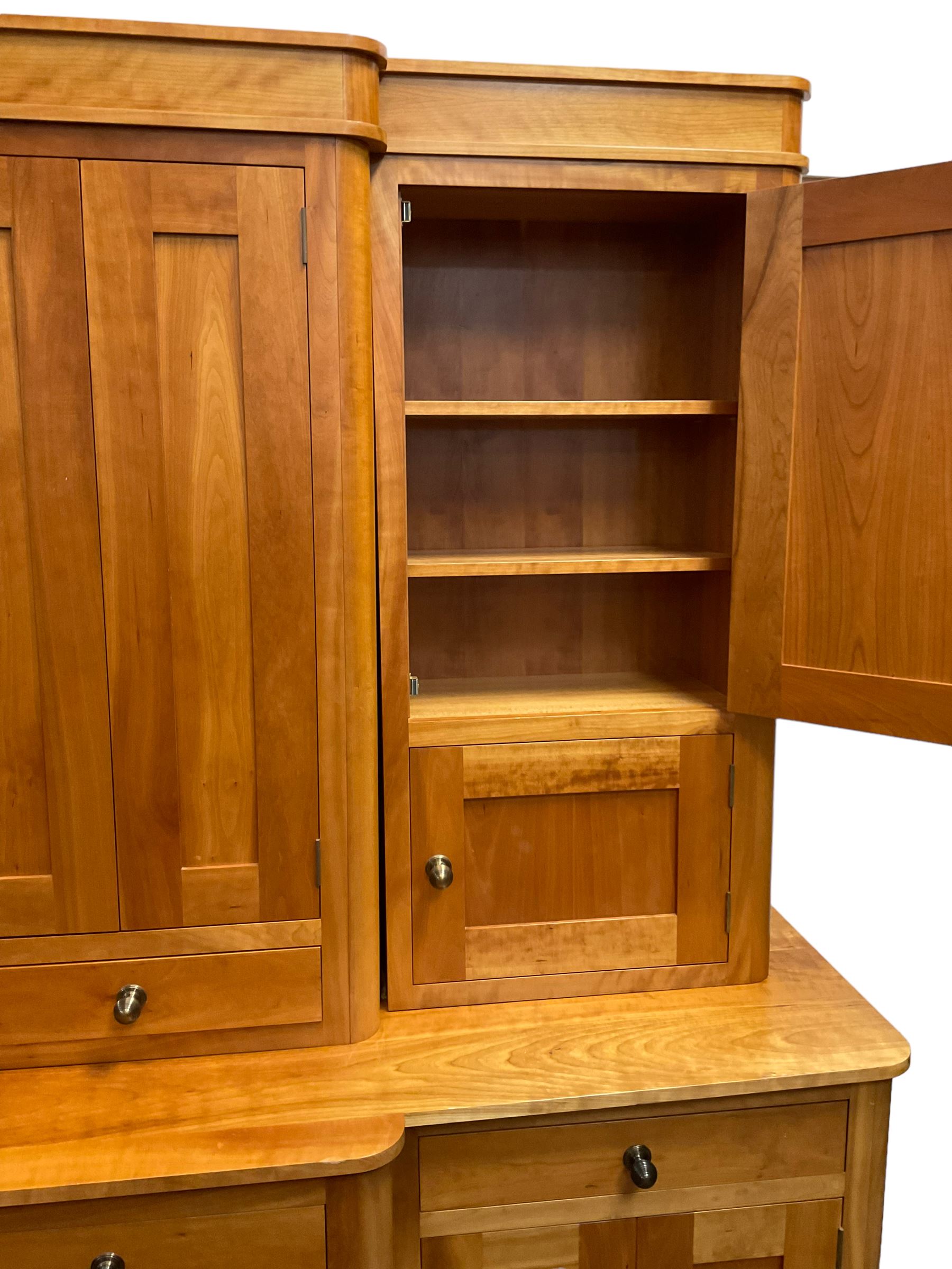 Large contemporary cherry wood break-front wall unit, the banded cornice over double cupboard with bifold doors and two drawers, flanked by four single cupboards, the base fitted with four drawers over four cupboards (W263cm, H216cm, D68cm); and a cherry wood cabinet, fitted with double cupboard over two short and two long drawers, with faux drawer facias (W81cm, H138cm, D66cm)