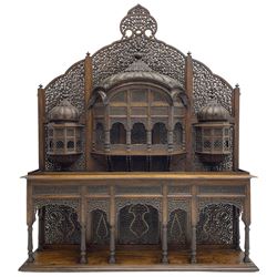 Late 19th century Indian Burmese carved and pierced hardwood and brass inlaid wall shelf, the shaped back profusely decorated with trailing and interlaced foliage, with projecting architectural structures, the central balcony with canopy top and five open windows with arched apertures on columns, two flanking five-sided balconies, the shelf supported by six foliate carved columns with pierced cusped pointed arches 