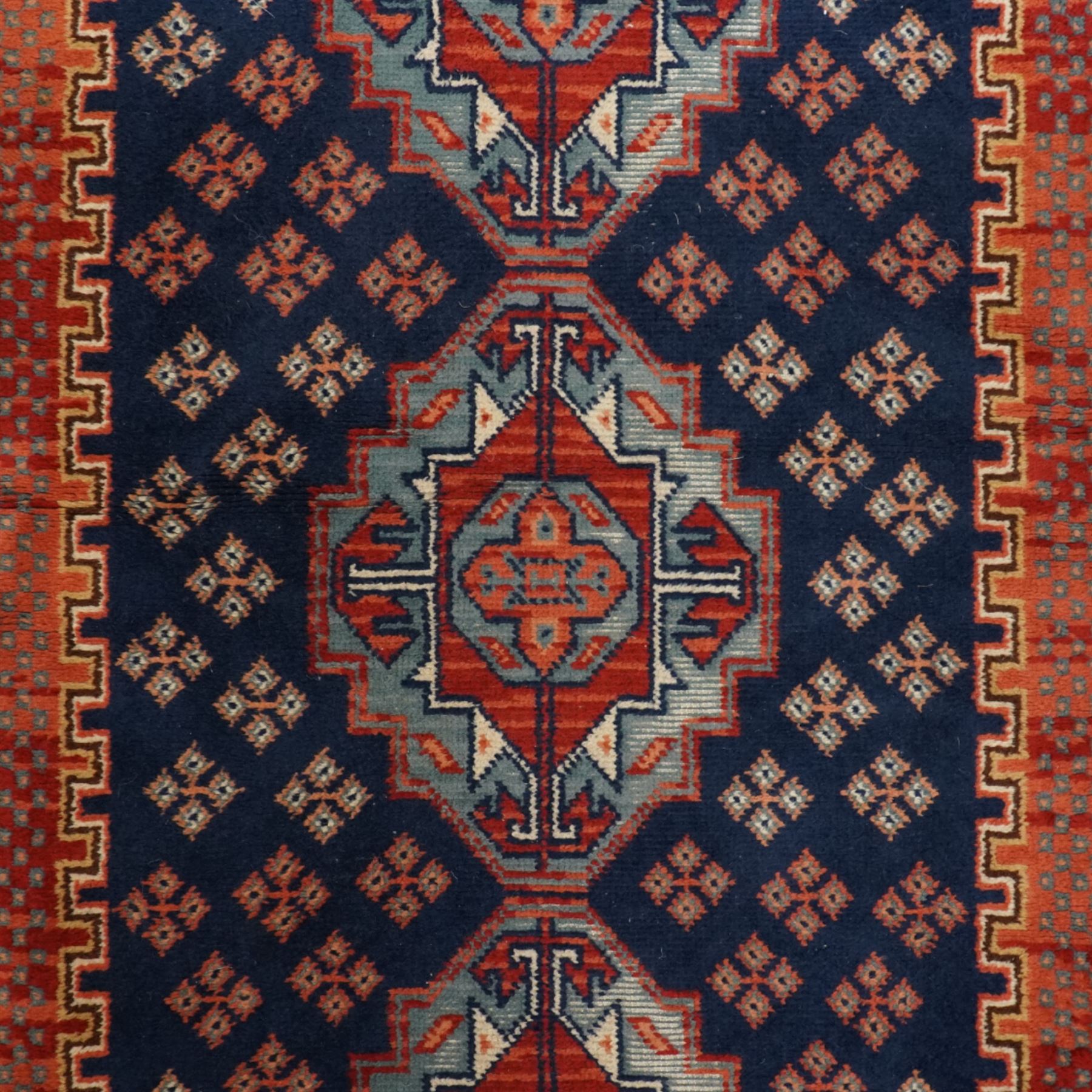 North West Persian Heriz hand-knotted rug, indigo field with three central stepped geometric medallions arranged vertically, enclosed by angular spandrels and multiple geometric borders in shades of madder red, ivory, and pale blue, with cotton fringe ends  
